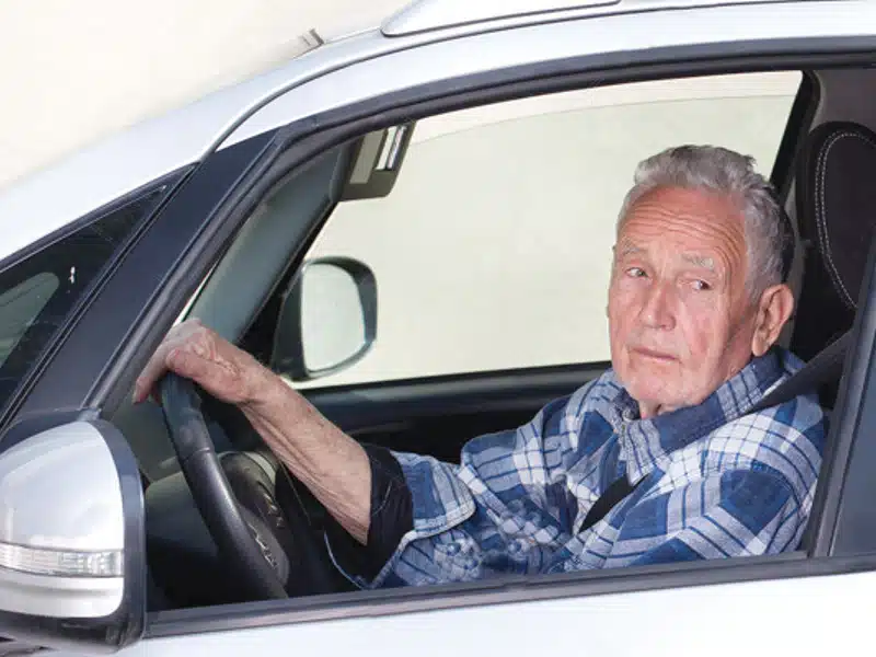 senior man driving a car looking out window